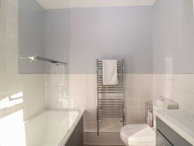A bathroom with a bathtub shower combo towel rack toilet and vanity at South Hill Farmhouse in Stow-On-The-Wold
