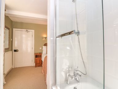 A bathroom with a bathtub and shower next to a bedroom with a bed and wooden nightstand at South Hill Farmhouse in Stow-On-The-Wold