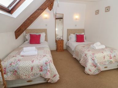 A bedroom with two single beds with floral quilts and a small wooden bedside table between them at South Hill Farmhouse in Stow-On-The-Wold