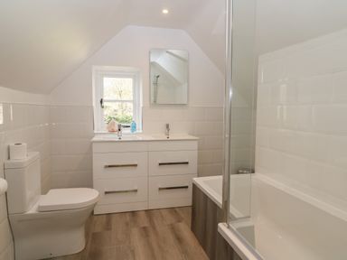 A bathroom with toilet, double sink vanity, mirror, window, and bathtub with glass shower screen at South Hill Farmhouse in Stow-On-The-Wold