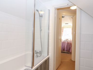 A bathroom with a bathtub and showerhead looking into a bedroom with a bed covered by a purple blanket at South Hill Farmhouse in Stow-On-The-Wold