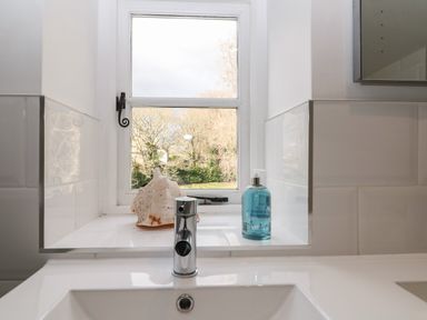 A bathroom sink with a chrome faucet and a window ledge holding a seashell and a blue liquid soap dispenser at South Hill Farmhouse in Stow-On-The-Wold