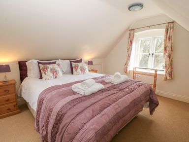 A bedroom with a double bed with folded towels bedside tables with lamps and a window with floral curtains at South Hill Farmhouse in Stow-On-The-Wold