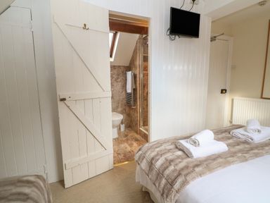 A bedroom with a bed covered with folded towels a television on the wall and a door leading to a bathroom at South Hill Farmhouse in Stow-On-The-Wold