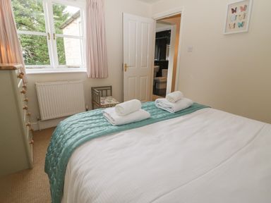A bedroom with a bed with towels on it a chair a dresser and an open door showing a bathroom at South Hill Farmhouse in Stow-On-The-Wold