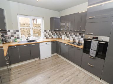 A kitchen with grey cabinets wooden countertops a dishwasher oven and a window showing a stone wall at South Hill Farmhouse in Stow-On-The-Wold