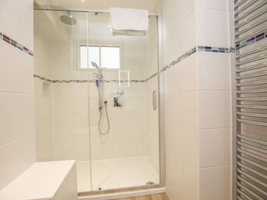 A bathroom with a glass shower enclosure a handheld showerhead a towel hanging and a heated towel rail at 5 Burford Mews in Burford