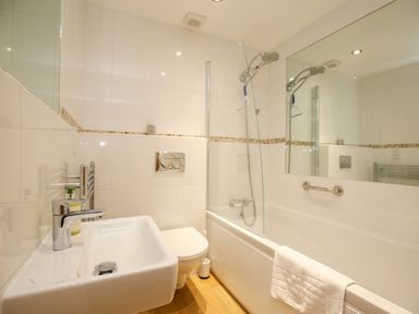 A bathroom with a sink, toilet, bathtub, shower, and mirror at 5 Burford Mews in Burford