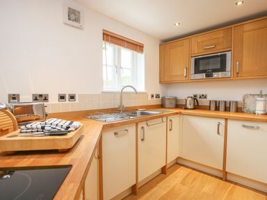 A kitchen with wooden countertops white cabinets a sink toaster kettle and microwave at 5 Burford Mews Burford