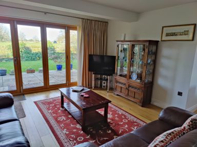 A living room with a wooden coffee table and glass cabinet next to large sliding doors opening to a garden at 5 Burford Mews in Burford