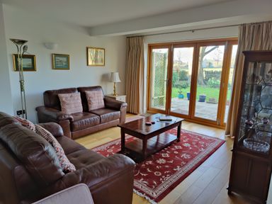A living room with two brown leather sofas a wooden coffee table a red patterned rug framed pictures on the wall and glass doors leading outside at 5 Burford Mews in Burford