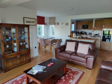 A living room with leather sofas a wooden coffee table and a display cabinet next to a dining area and kitchen at 5 Burford Mews in Burford