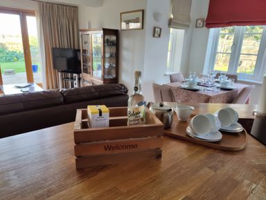 A kitchen counter with a wooden crate labeled welcome holding a bottle and a box a tray with teacups a teapot and a creamer in a living and dining room at 5 Burford Mews in Burford