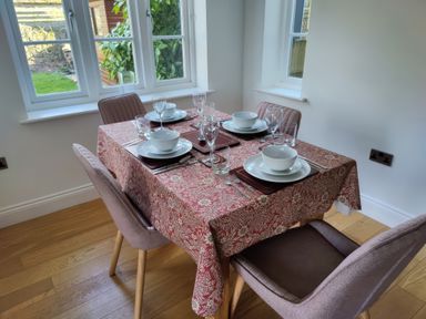 A dining area with a wooden table covered by a patterned tablecloth set for four with bowls glasses and cutlery at 5 Burford Mews in Burford