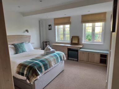 A bedroom with a bed a desk two windows and storage at 5 Burford Mews in Burford