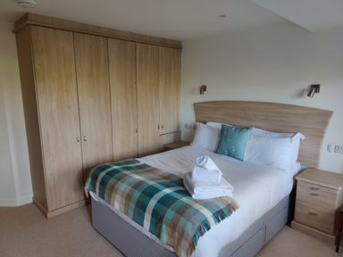 A bedroom with a bed with a blue and green checkered blanket and wooden wardrobes and bedside tables at 5 Burford Mews in Burford