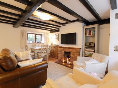 A living room with a brown leather sofa white armchairs dining table and brick fireplace at One Masons Court in Stratford upon Avon