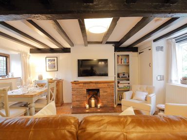 A living room with exposed beams a brick fireplace a TV a dining table and chairs at One Masons Court in Stratford upon Avon