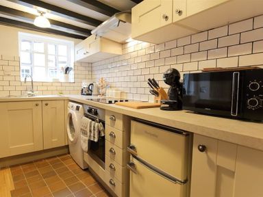 A kitchen with cream cabinets white tiled backsplash microwave coffee maker and a washing machine at One Masons Court in Stratford upon Avon