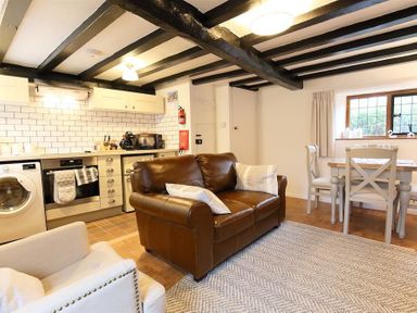 A living area with a brown leather sofa white armchair dining table and kitchen appliances at One Masons Court in Stratford upon Avon