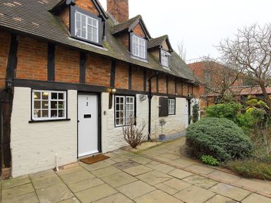 A brick and timber framed house with white doors and windows and a garden with shrubs and trees at One Masons Court in Stratford upon Avon