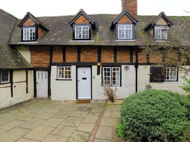 An exterior view of a brick and timber cottage with a tiled roof and paved courtyard at One Masons Court in Stratford upon Avon