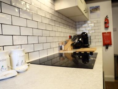 A kitchen countertop with a stove a coffee machine jars labeled coffee and sugar and a fire extinguisher on the wall at One Masons Court in Stratford upon Avon
