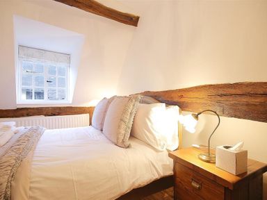 A bedroom with a bed beside a wooden nightstand with a lamp and tissue box at One Masons Court in Stratford upon Avon