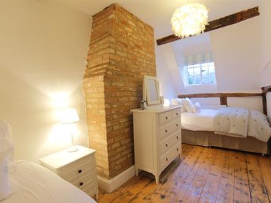 A bedroom with wooden floor white dressers a bed and an exposed brick chimney at One Masons Court in Stratford upon Avon