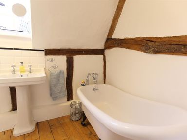 A bathroom with a white bathtub and sink wooden beams on walls and wooden floor at One Masons Court in Stratford upon Avon
