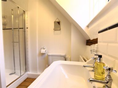 A bathroom with a sink and soap dispenser next to a toilet and a glass shower at One Masons Court in Stratford upon Avon
