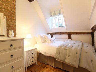 A bedroom with a bed pillows bedside table lamp chest of drawers and a window at One Masons Court in Stratford upon Avon