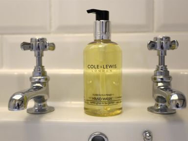A hand wash bottle between two chrome taps on a white sink at One Masons Court in Stratford upon Avon