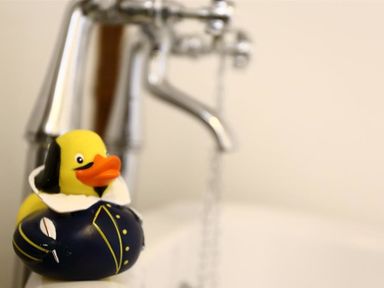 A rubber duck dressed as a historical figure beside a silver faucet over a white sink at One Masons Court in Stratford upon Avon