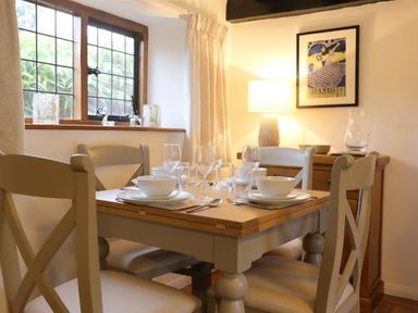 A dining area with a wooden table set with bowls glasses and cutlery and four chairs near a window and a framed picture at One Masons Court in Stratford upon Avon