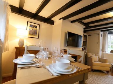 A dining area with a set table including bowls glasses and cutlery near a TV and armchair at One Masons Court in Stratford upon Avon