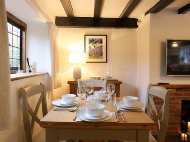 A dining table set for four with white dishes and glassware in a room with exposed beams and a brick fireplace at One Masons Court in Stratford upon Avon