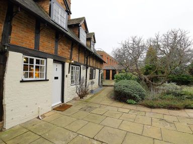 A pathway with bushes and trees beside a brick house with white doors and windows at One Masons Court in Stratford upon Avon