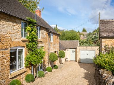 A stone house with white windows a gravel driveway and a garage door at Orchard House in Stow-On-The-Wold