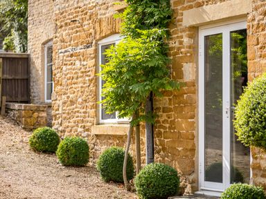A stone house exterior with white framed windows and door and round green bushes at Orchard House in Stow-On-The-Wold