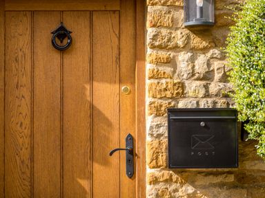 A wooden front door with a black handle and knocker next to a black mailbox on a stone wall