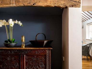 A carved wooden cabinet with a flower pot a brass object and a basket on top at Orchard House in Stow-On-The-Wold