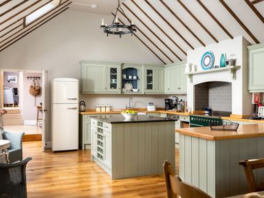 A kitchen with green cabinets a central island refrigerator and wooden flooring at Orchard House in Stow-On-The-Wold