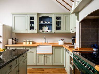 A kitchen with cream cabinets a white sink a stove and various kitchen items on counters at Orchard House in Stow-On-The-Wold