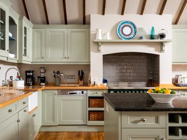 A kitchen with green cabinets wooden countertops a black countertop island and kitchen appliances at Orchard House in Stow-On-The-Wold