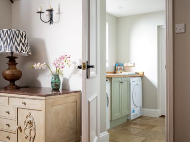 A wooden cabinet with a lamp and vase with flowers next to a doorway leading to a laundry room with washing machine and dryer at Orchard House in Stow-On-The-Wold