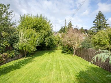 A garden with a mowed lawn surrounded by trees and a woven fence at Orchard House in Stow-On-The-Wold