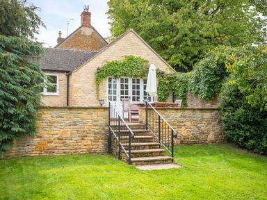 A stone house with a grassy yard and a patio with outdoor furniture at Orchard House in Stow-On-The-Wold