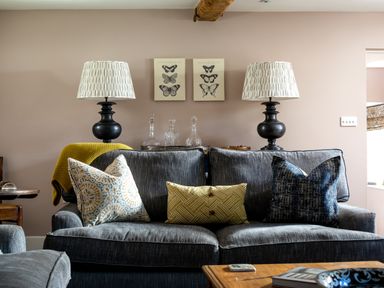 A living room with a gray sofa with patterned cushions two black lamps with patterned shades and butterfly artwork on the wall at Orchard House in Stow-On-The-Wold