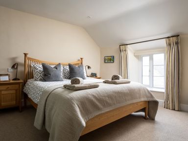 A bedroom with a wooden bed frame pillows bedside tables lamps and a window with curtains at Orchard House in Stow-On-The-Wold